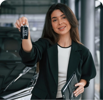 Een glimlachende vrouw in een autoshowroom houdt de autosleutels naar voren en gebaart zelfverzekerd. Ze draagt een zwarte blazer en houdt een tablet vast, terwijl ze naast een glanzende zwarte auto staat.