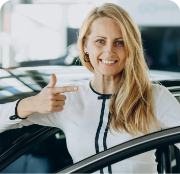 Een glimlachende vrouw in een autoshowroom houdt een creditcard omhoog, wijst er met één hand naar en straalt enthousiasme en zelfvertrouwen uit terwijl ze naast een zwarte auto staat.